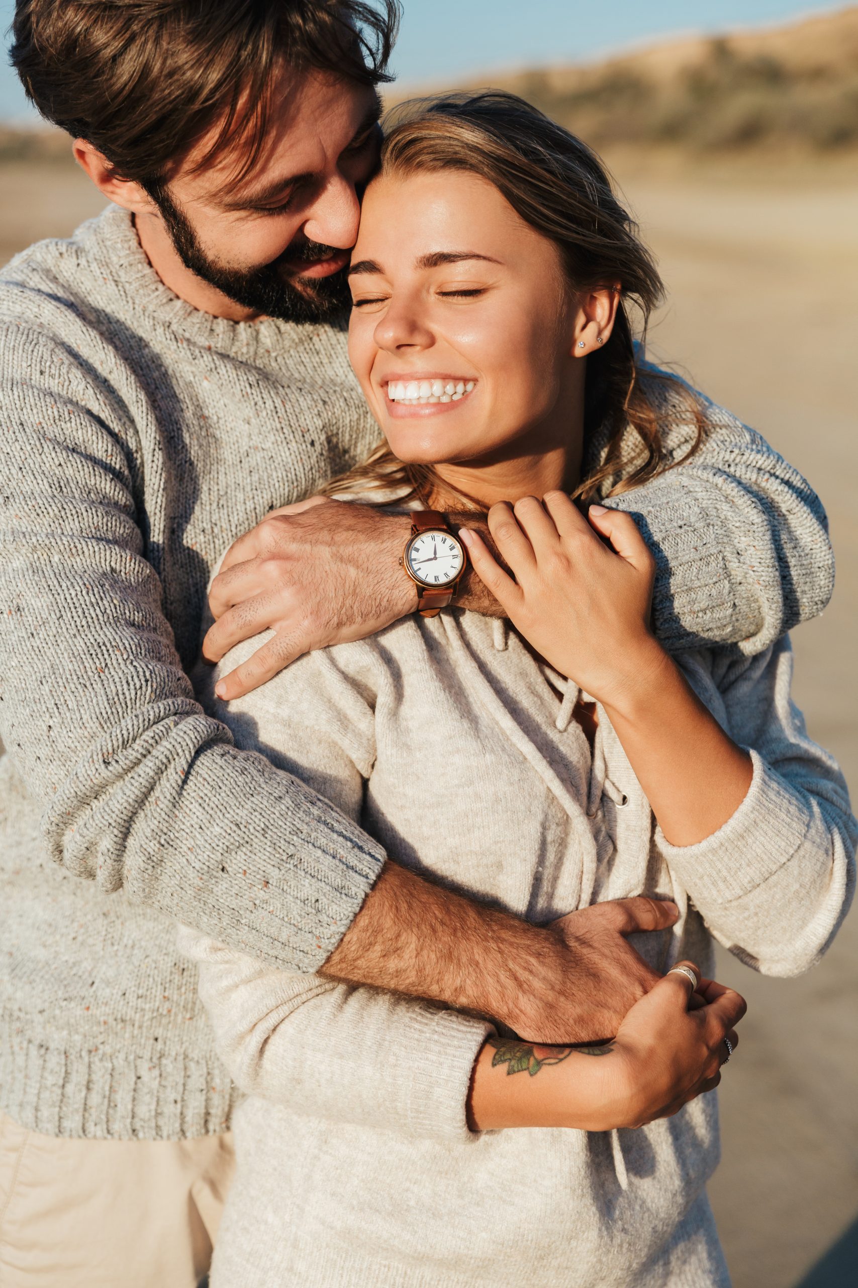 Photo of young pleased smiling happy loving couple outdoors at beach hugging.