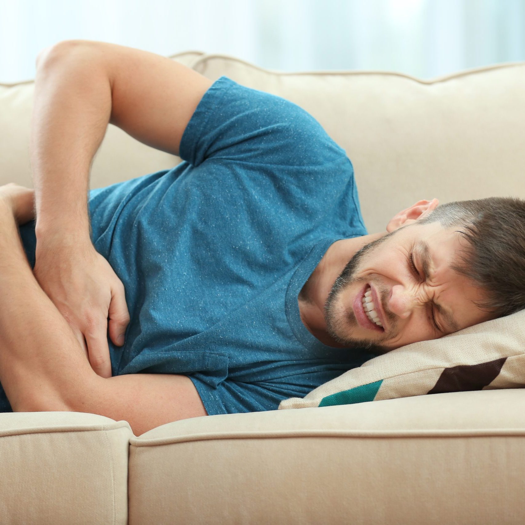 Handsome young man suffering from stomach ache while lying on sofa at home