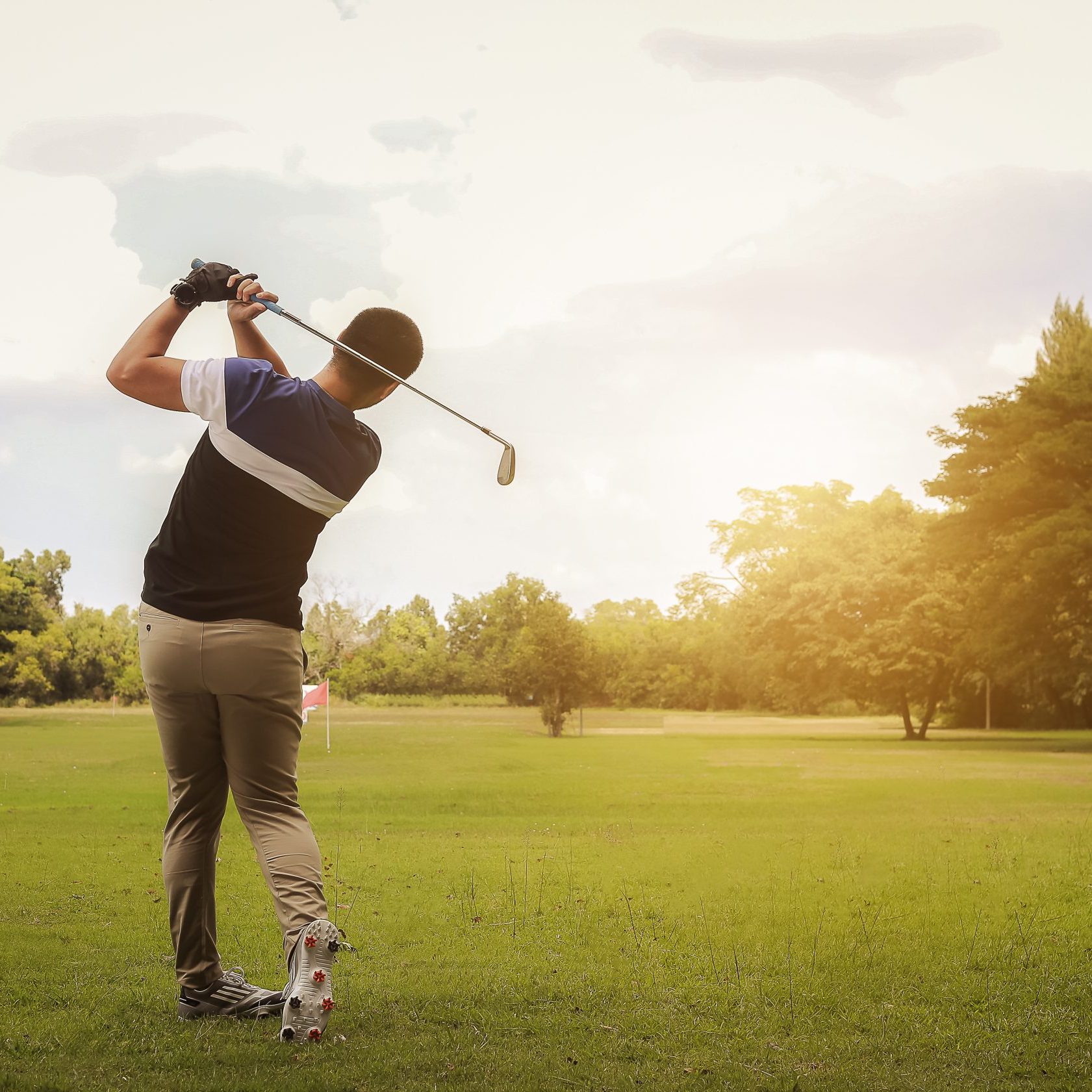 Golfer hitting golf shot with club on course at evening time.