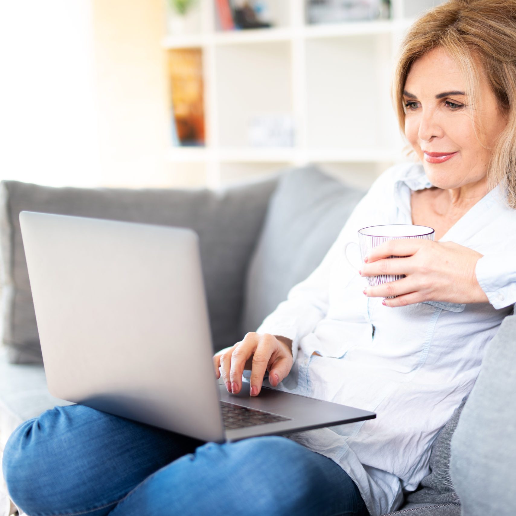 Ältere Dame sitzt gemütlich auf der Couch und schaut in ihren Laptop