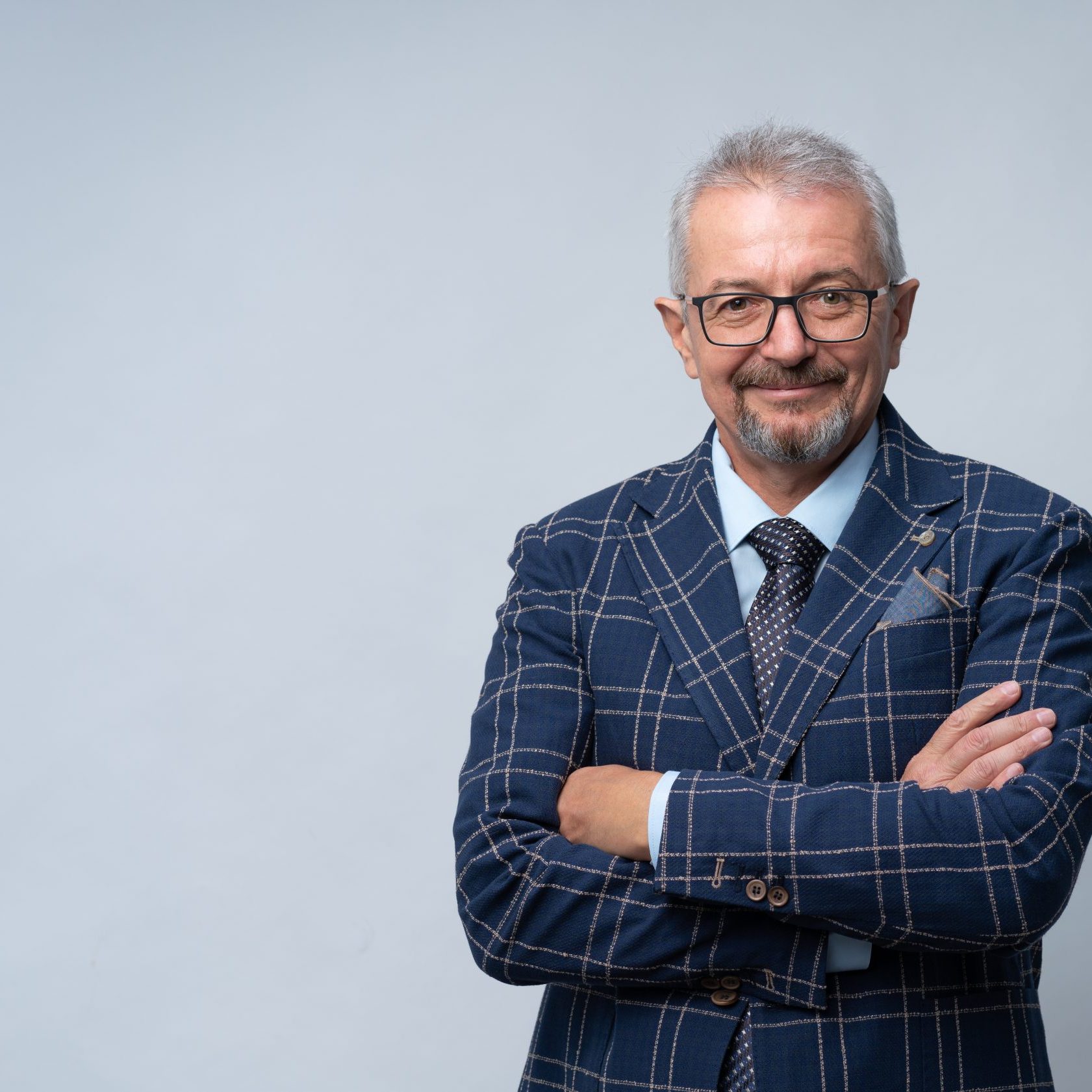 Smiling and happy mature man in glasses and a suit with crossed arms