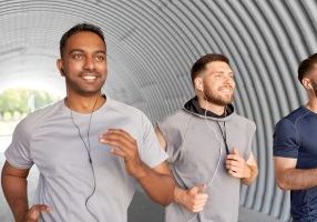 fitness, sport and healthy lifestyle concept - smiling young men or male friends with earphones running outdoors
