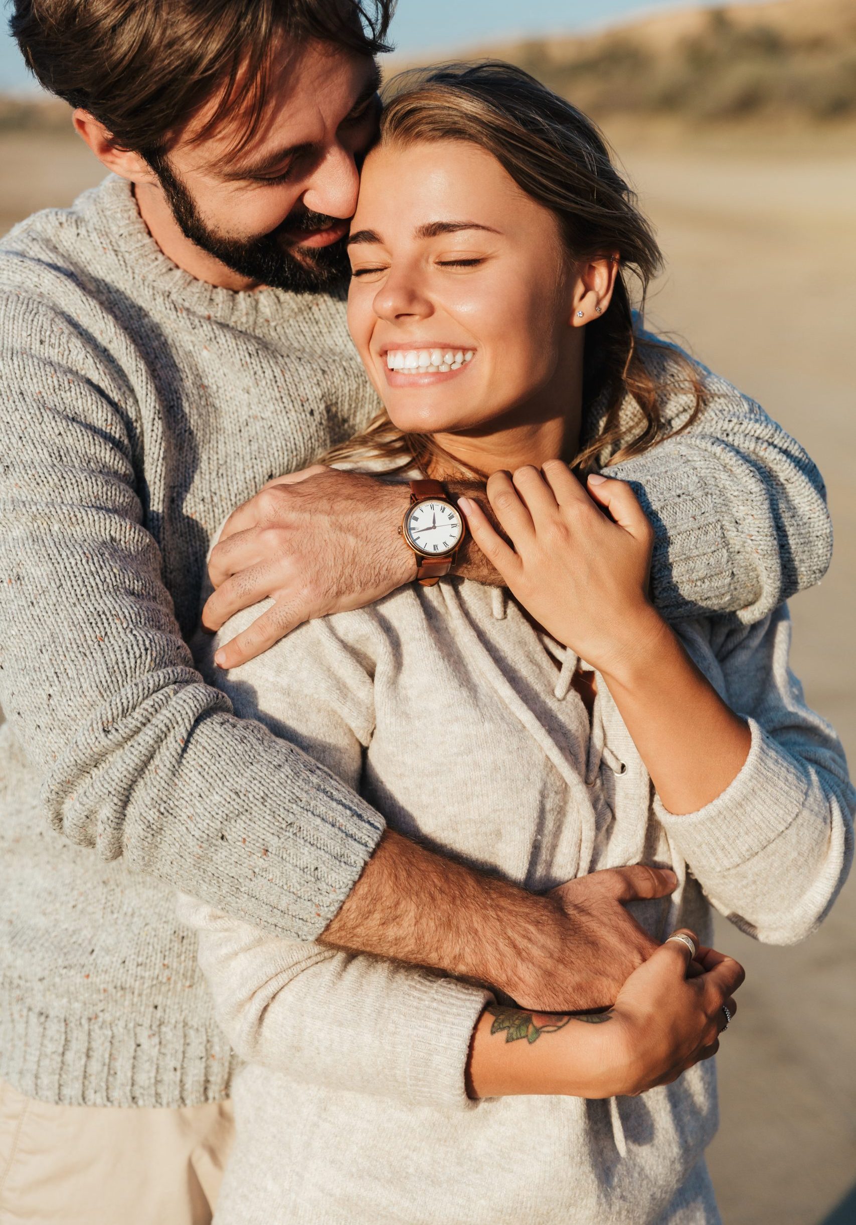 Photo of young pleased smiling happy loving couple outdoors at beach hugging.