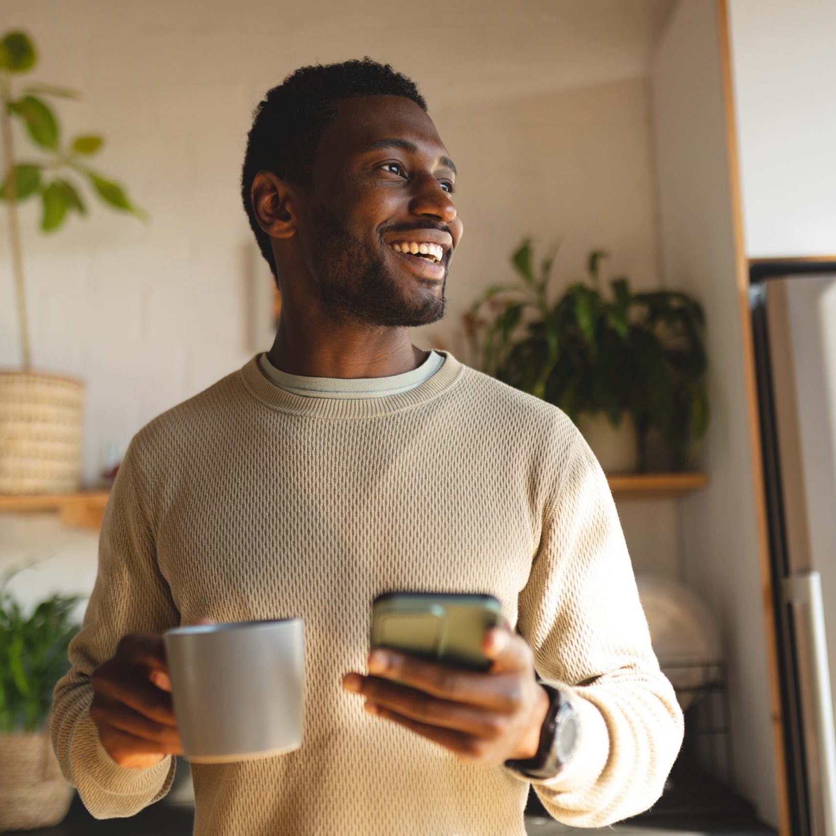 Happy african american man using smartphone and drinking coffee